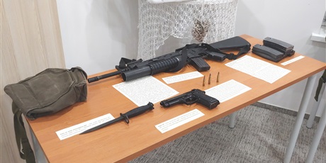 Powiększ grafikę: Na zdjęciu stół, na którym leży replika pistoletu Beretta i karabinu M16 oraz oryginalny bagnet M7, pokrowiec na maskę przeciwgazową i magazynki do karabinu M16.