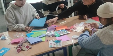 Powiększ grafikę: Na zdjęciu wychowanki siedzące przy stole na którym znajdują się materiały plastyczne potrzebne do wykonania kartek