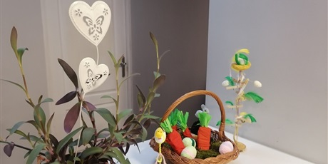 Powiększ grafikę: Dekoracje Wielkanocne kwiat doniczkowy oraz koszyczek z ozdobnymi marchewkami i pisankami.