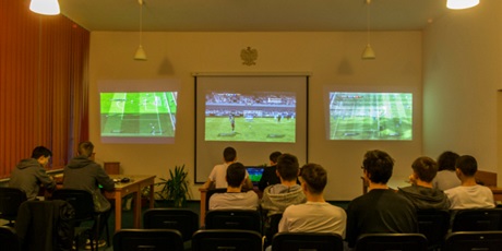 Powiększ grafikę: Zgromadzeni na widowni wychowankowie podziwiają trzy toczące się naraz mecze w Fifę. Obraz wyświetlany jest na ścianie dzięki projektorom.