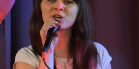 Powiększ grafikę: Zbliżenie na twarz młodej brunetki śpiewającej do mikrofonu.