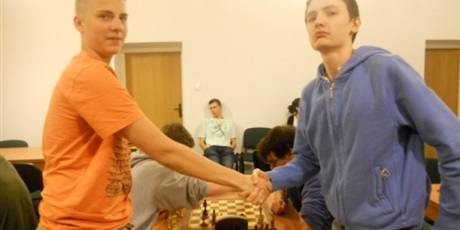 Powiększ grafikę: Sala w której obywają się rozgrywki szachowe. Na pierwszym planie dwóch zawodników podaje sobie ręce, za nimi trwa starcie szachistów